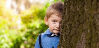 A shy kid standing behind the tree