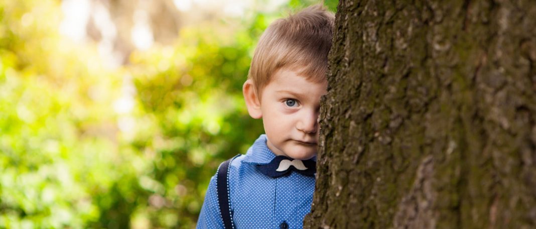 A shy kid standing behind the tree